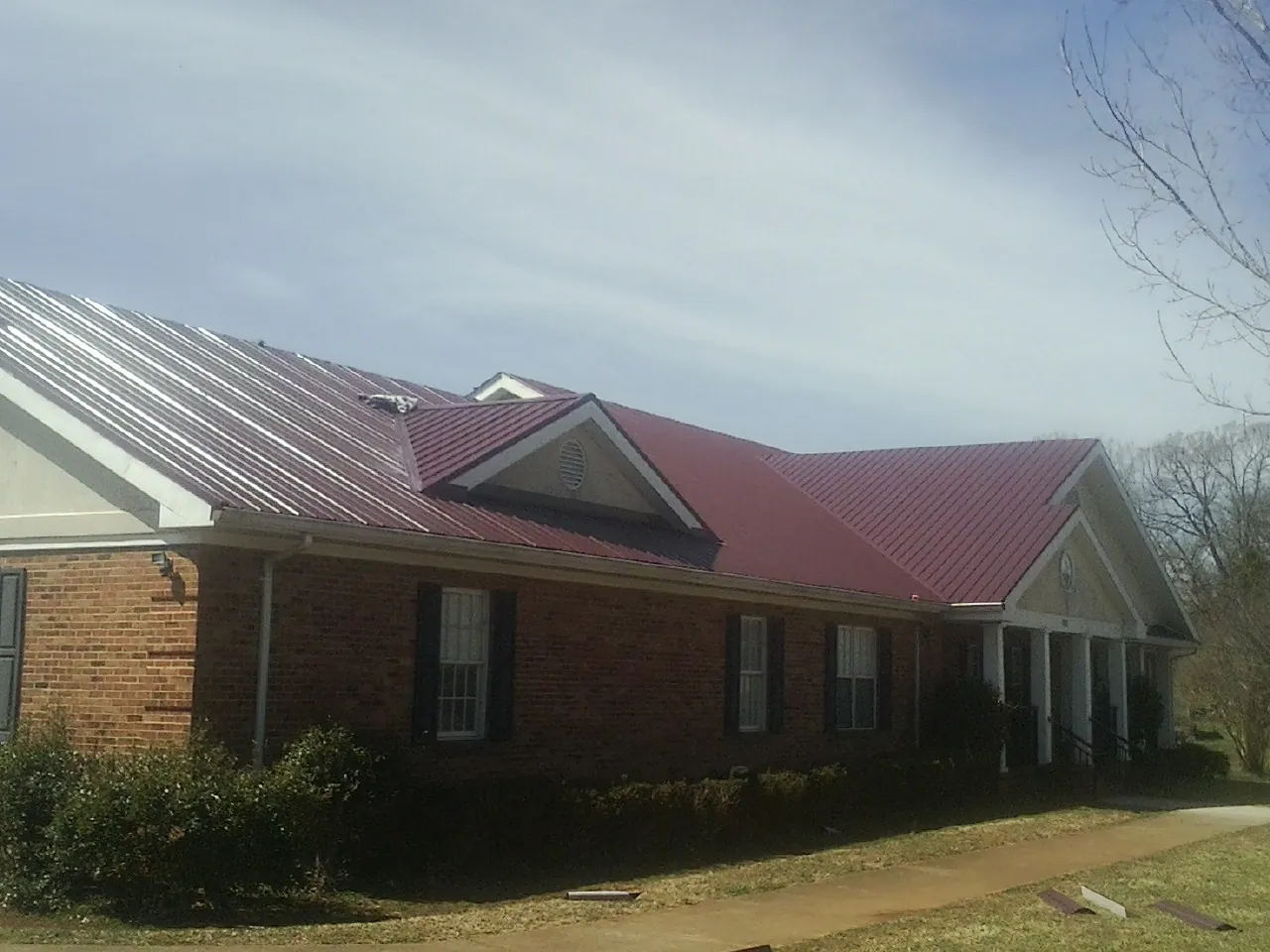 Red metal roof with gabled entries on a long brick building, from a Hail Damage Roof Repair job in West Middletown