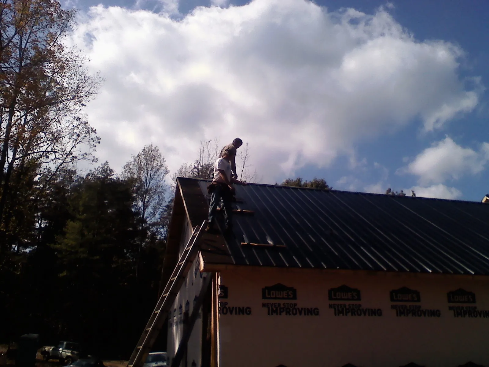 Roofer fastening dark metal panels high against a cloudy sky, from a Roof Inspection job in West Middletown