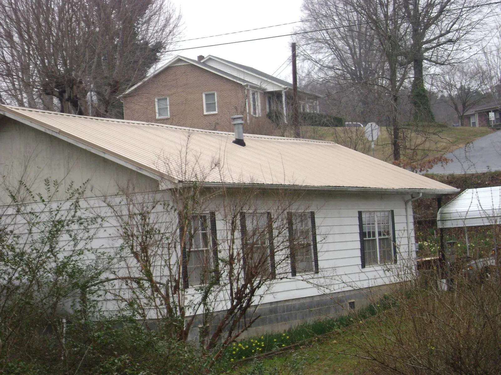 Tan metal roof on a white sided house set into a hillside — Commercial Roofing by Roofing Brothers in West Middletown